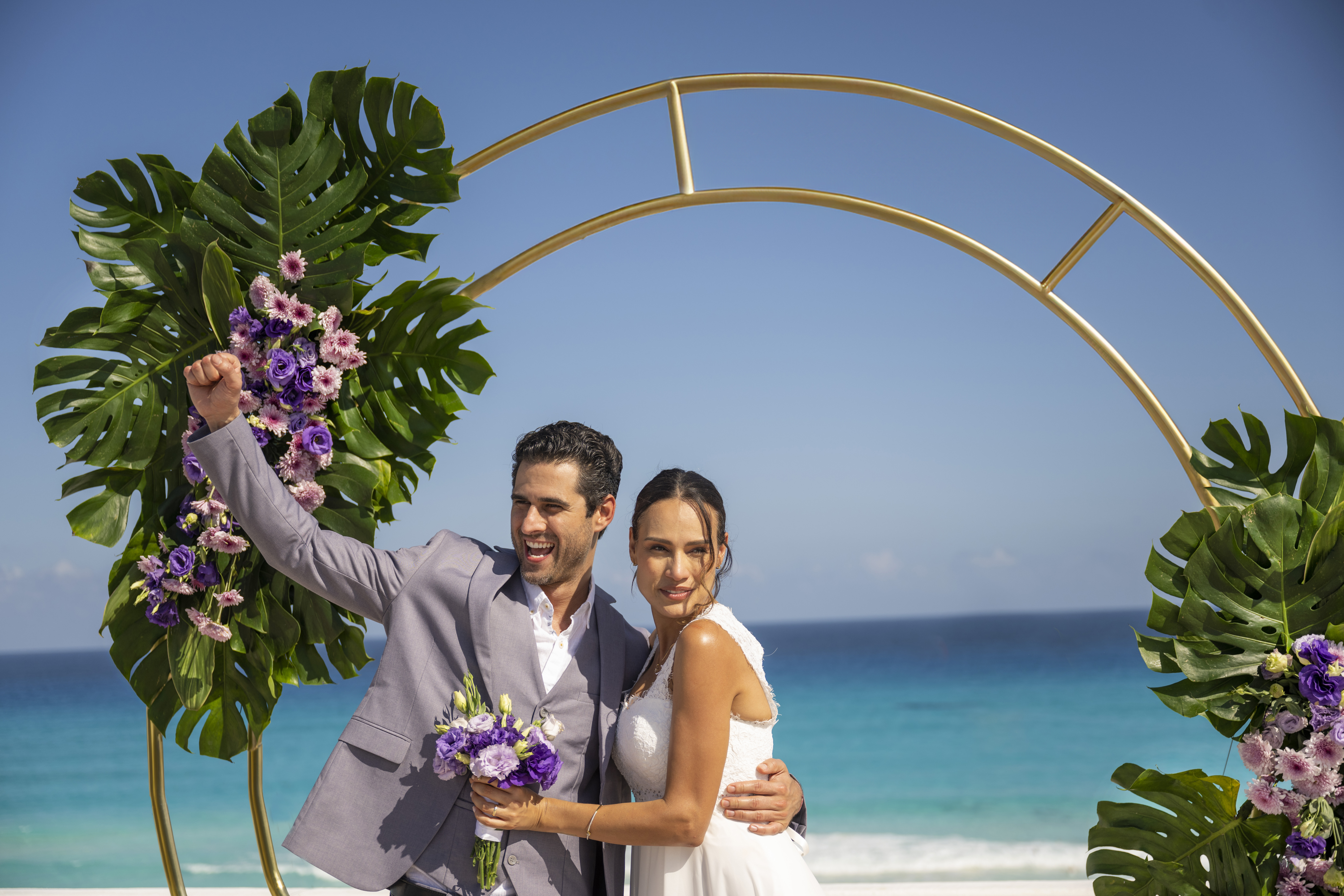 Newly married couple posing under a tropical wedding arch by the sea.