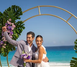 Newly married couple posing under a tropical wedding arch by the sea.