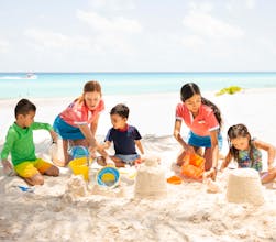 Kids building sandcastles together on a sunny beach with the sea in the background.